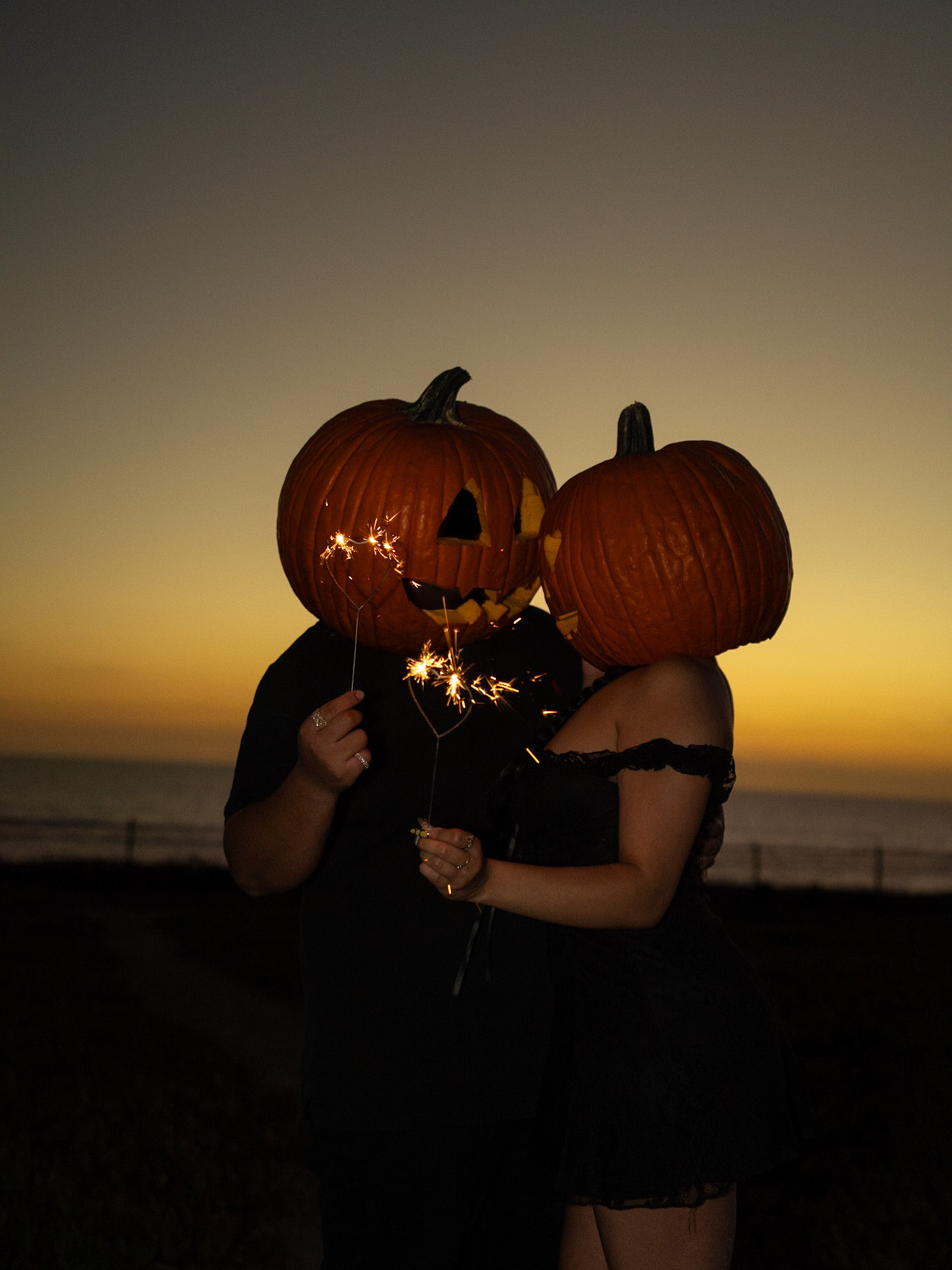 Couple wearing pumpkin masks and holding sparklers at sunset
